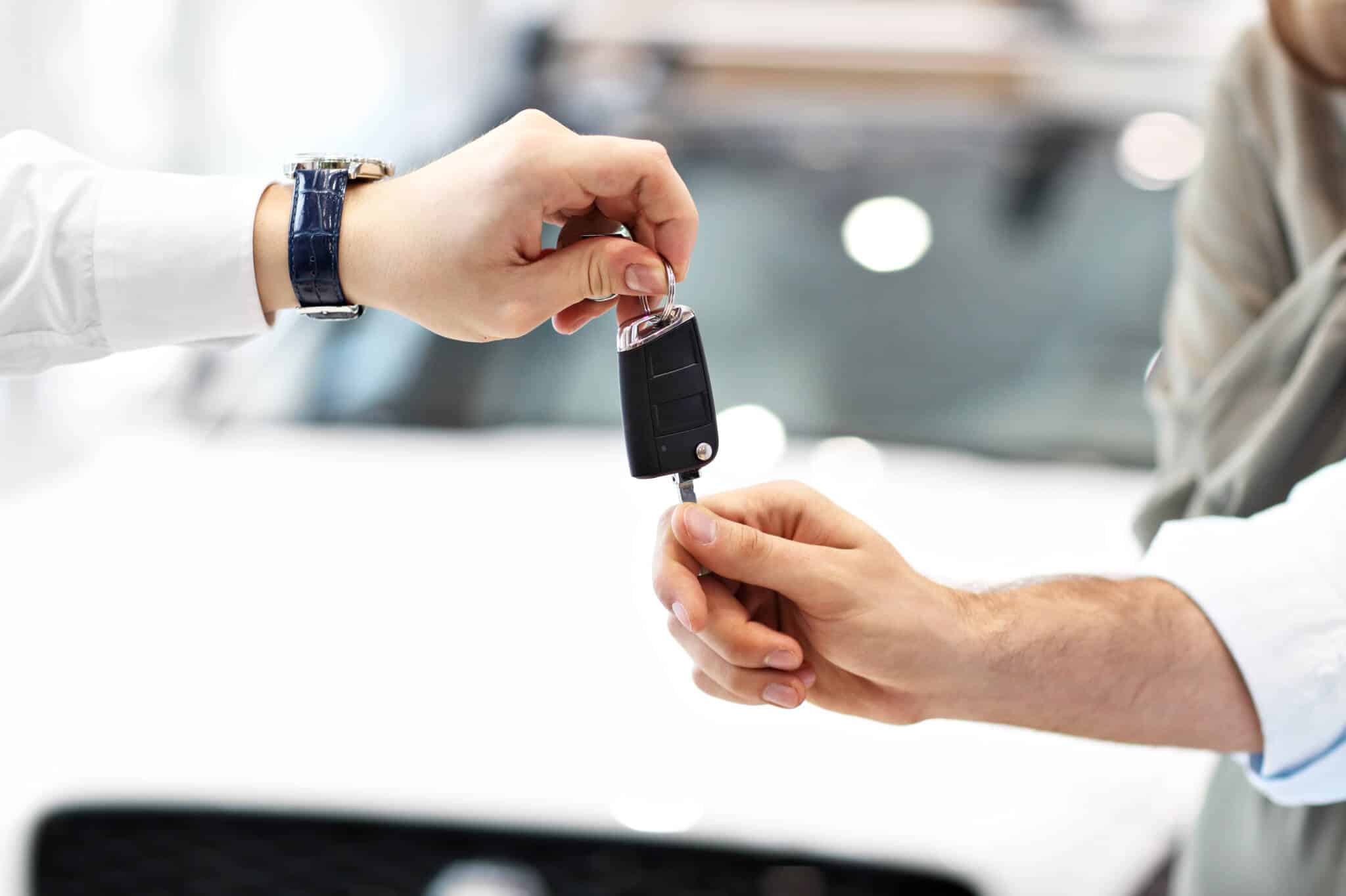 mãos de homem e mulher trocam chaves de carro em fundo desfiocado de um stand automóvel, no qual são praticadas s soluções Crédito automóvel, leasing ou renting