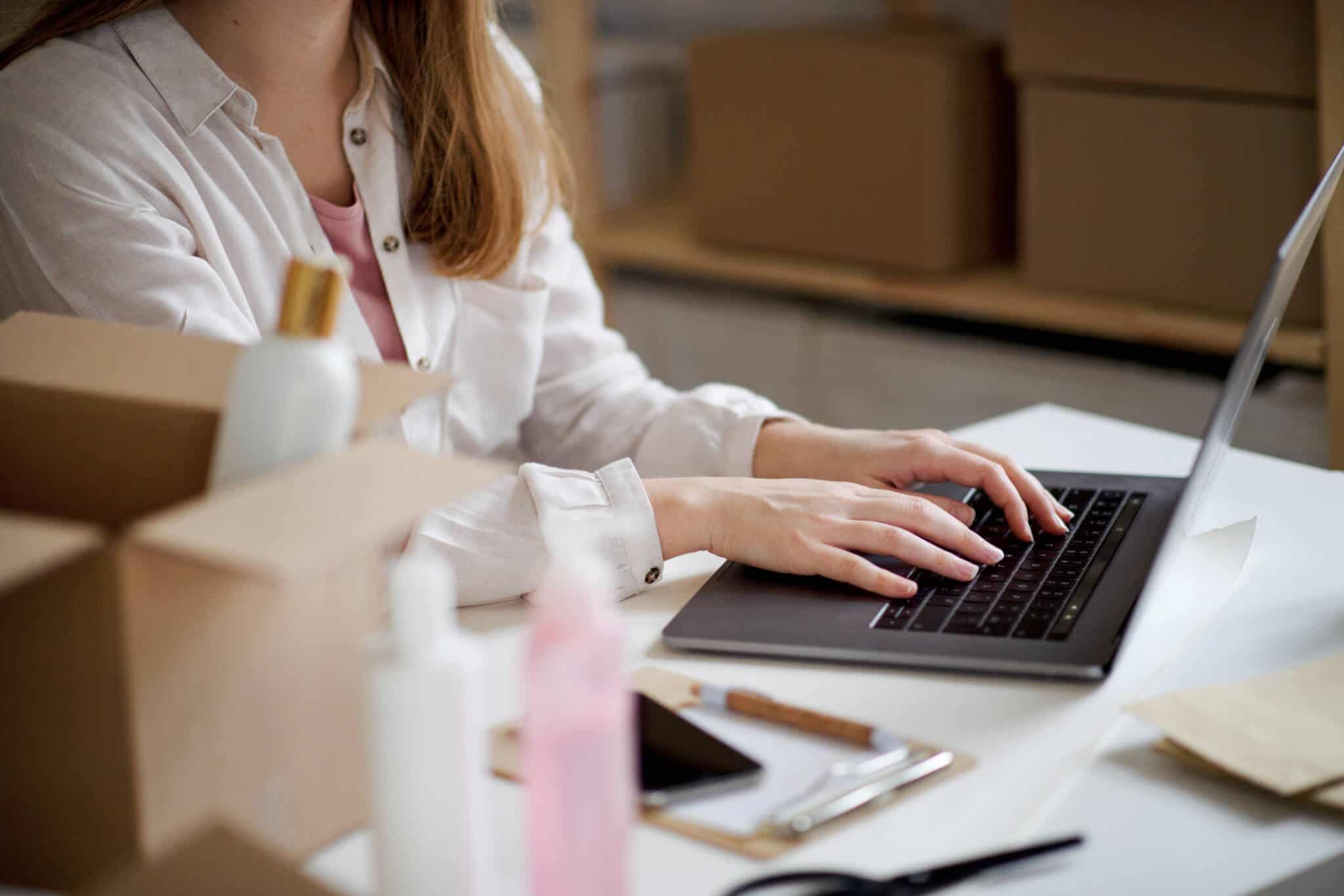 jovem mulher ao computador, numa sala rodeada de caixas, a desenvolver a sua atividade de dropshipping