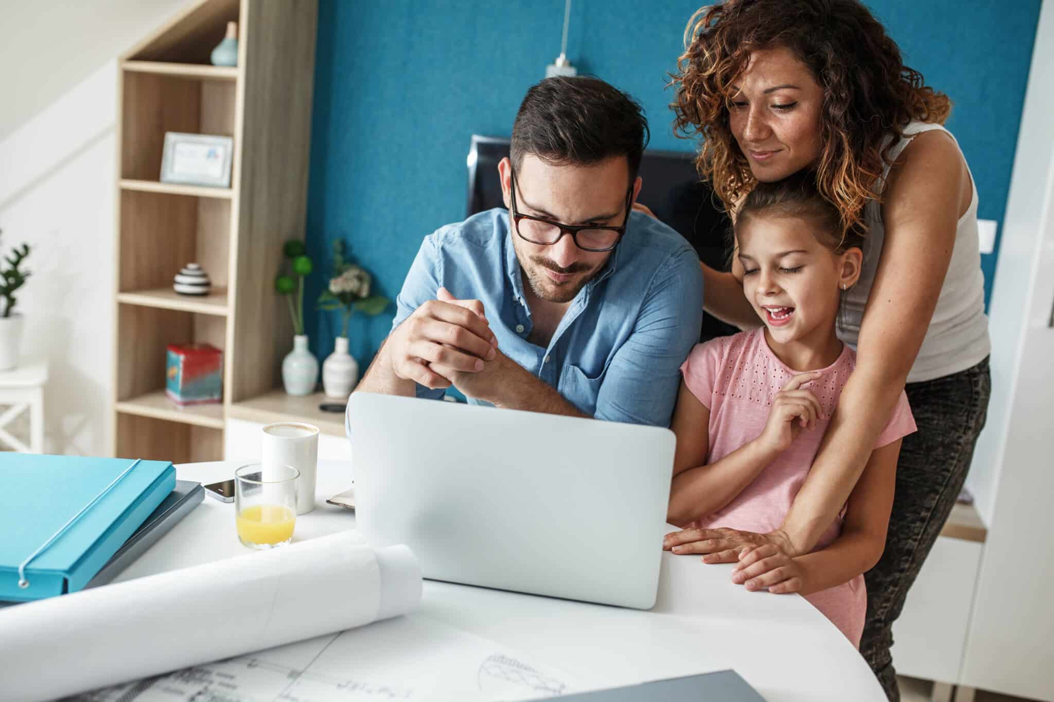 jovem casal e a sua filha , na sala e ao computador,fazem contas aos seus hábitos financeiros para que sejam mais saudáveis e consigam poupar