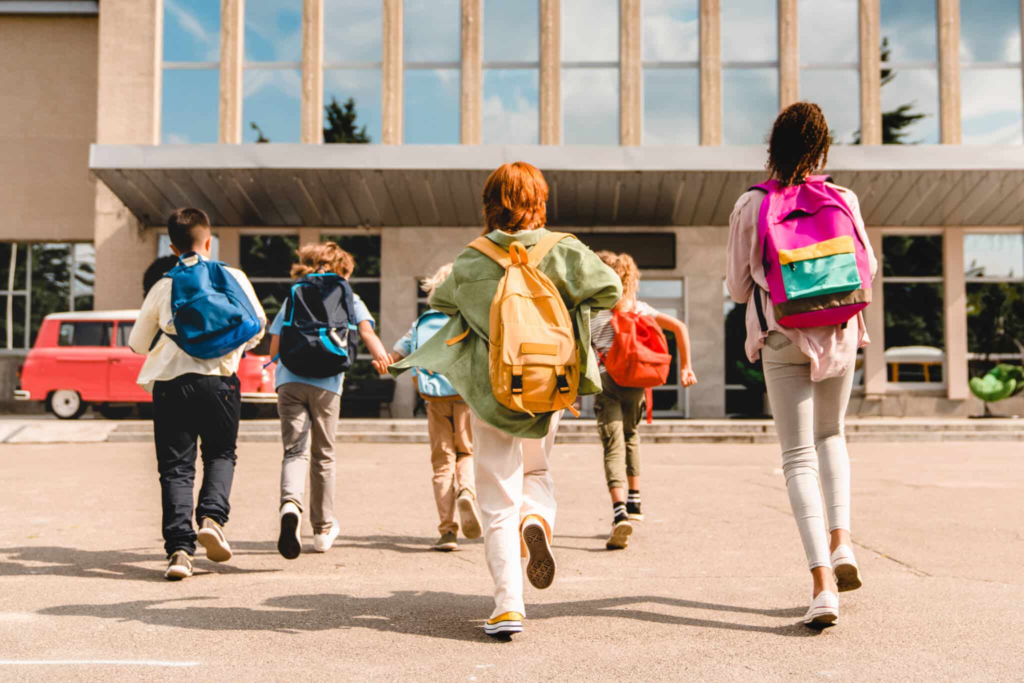 grupod e crianças, pre adolescentes, correm com as mochilas às costas á entrada da escola, da qual vão fazer transferência