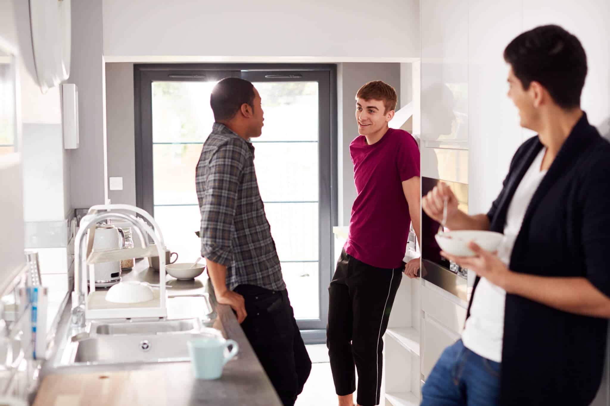 um espaço alojamento universitário com três rapazes estudantes, a conversar, comer e beber na cozinha