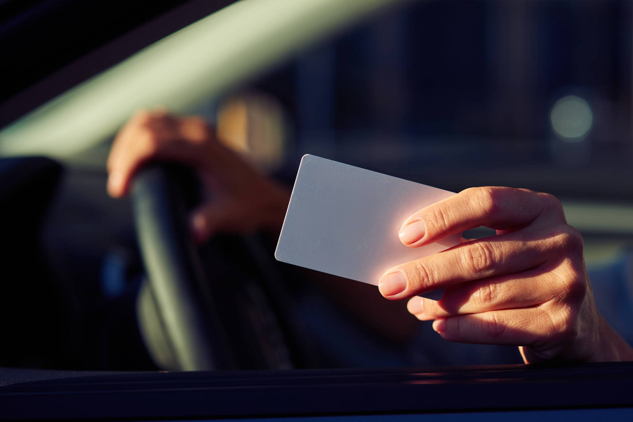 mão de jovem rapaz sentado no carro a conduzir estende à janela carta de condução que precisa de revalidar