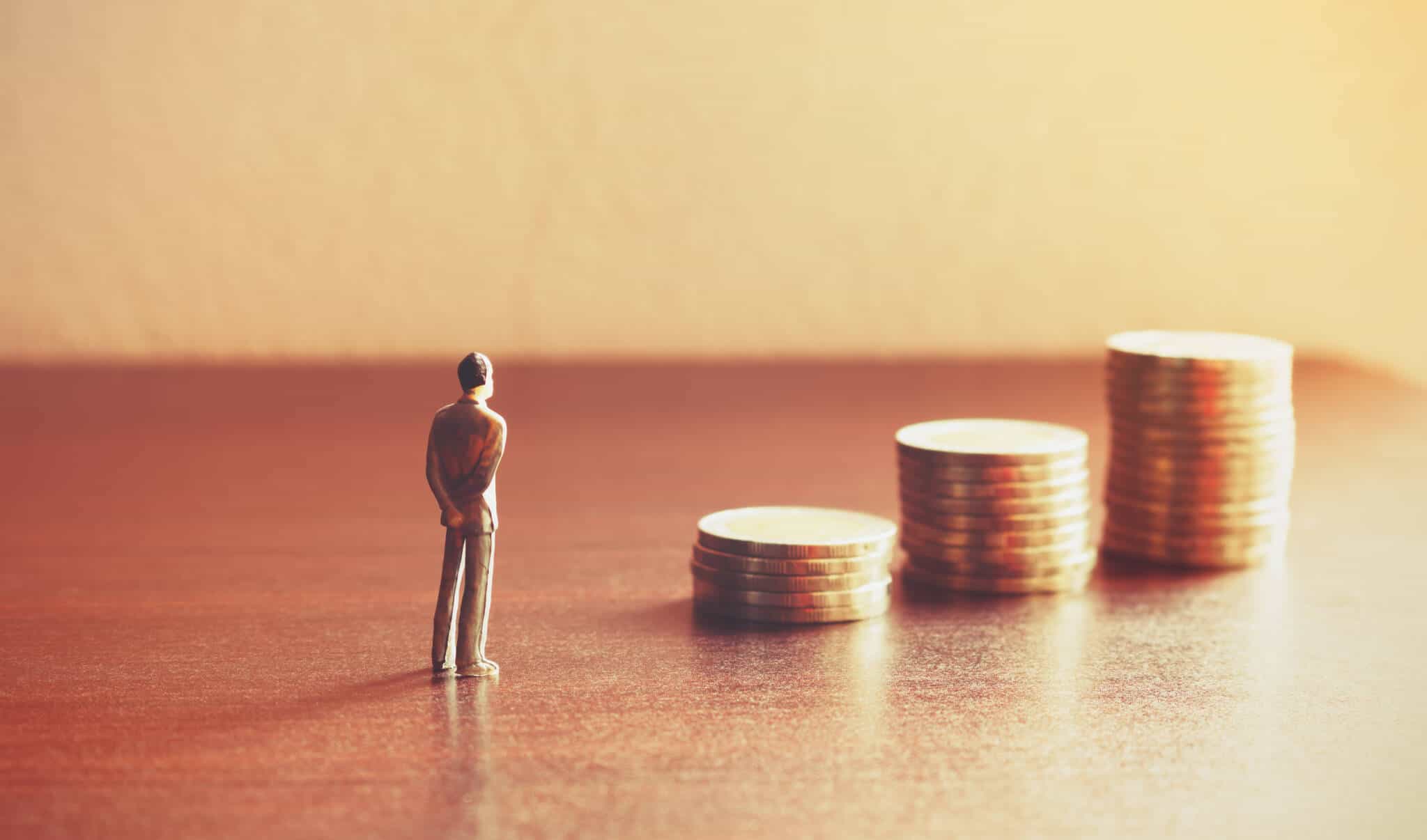pessoa em miniatura a olhar para pilha de moedas