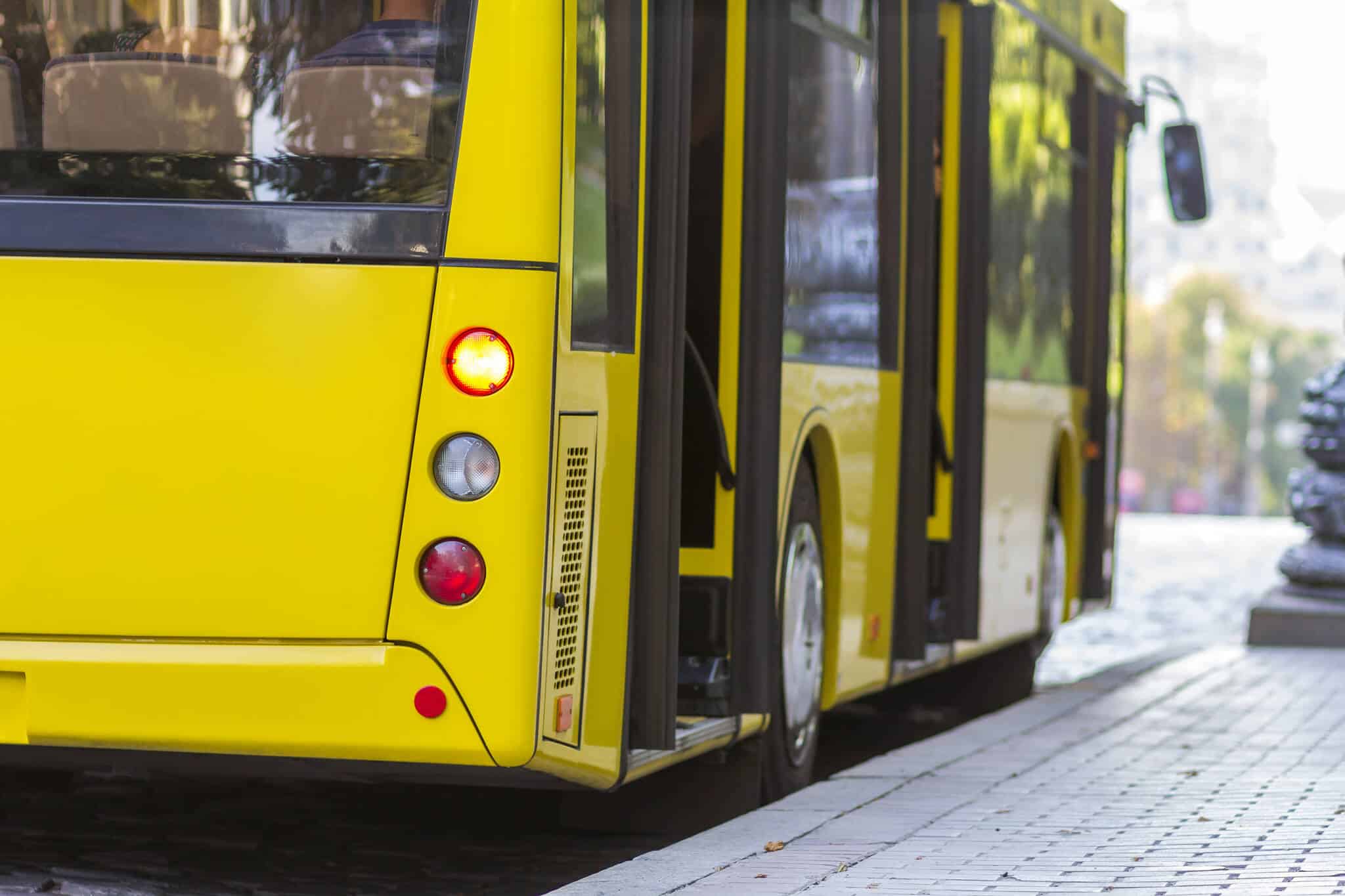 um dos Transportes públicos é o autocarro amarelo, moderno, e este está parado junto a uma paragem de autocarro no centro de uma cidade