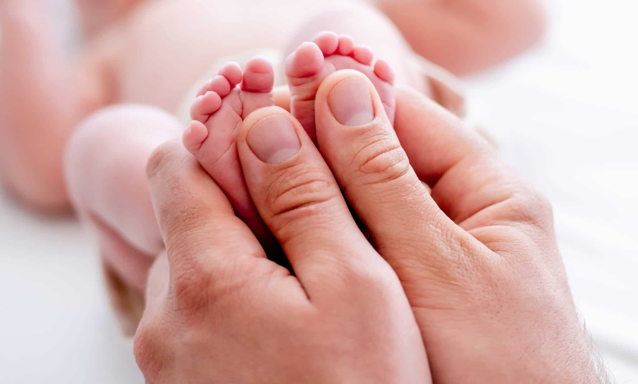 mãos agarram pés de recém nascido deitado de barriga para cima, em fundo desfocado
