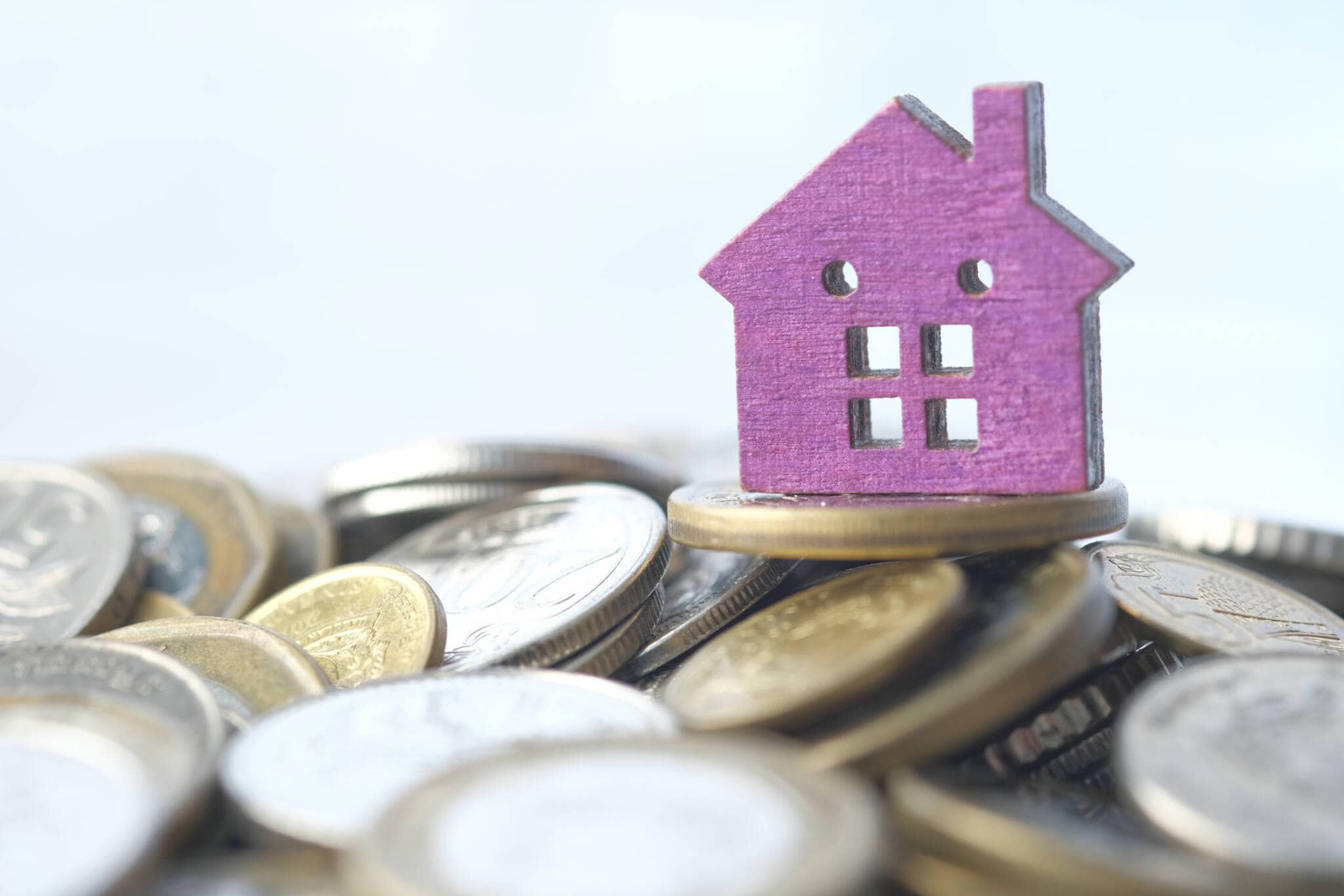 pilha de moedas de euro espalhadas com uma casa apenas com fachada, roxa, no topo simbolizando a isenção de IMI