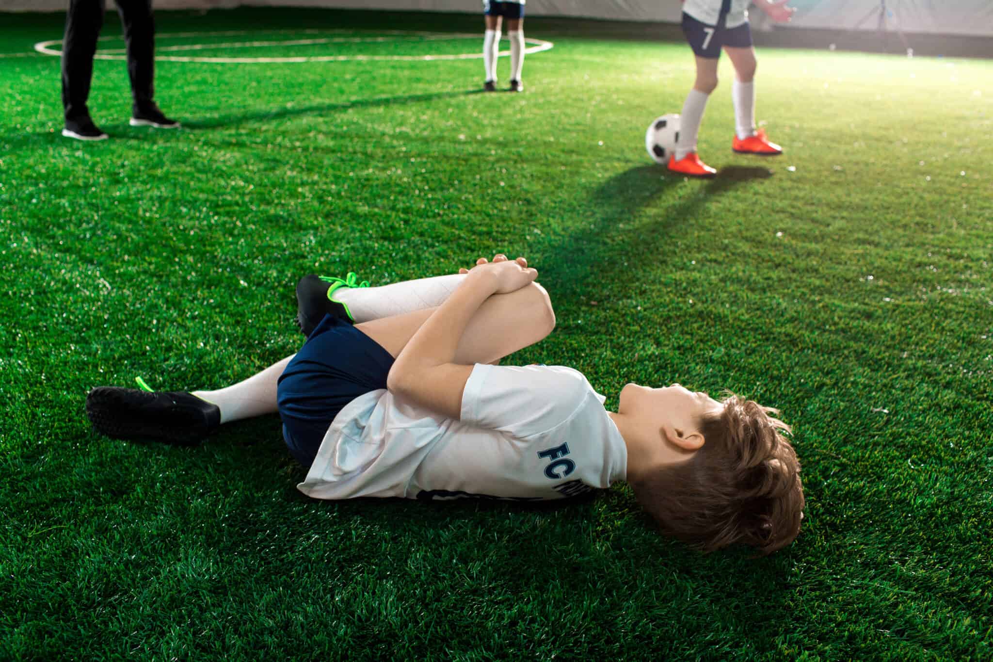 criança deitada no relvado num jogo de futebol, o seu desporto que pratica com seguros