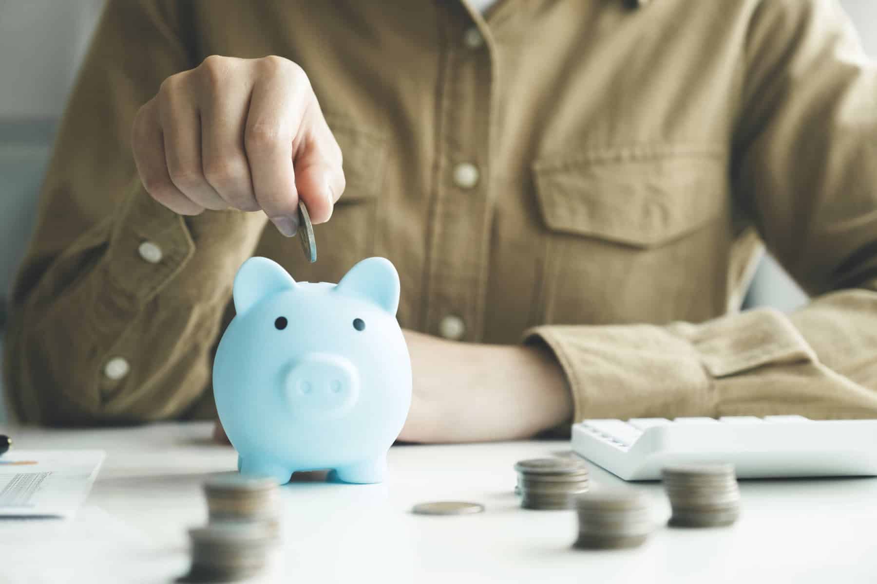 pessoa a colocar moedas num porquinho mealheiro a ilustrar a criação de um fundo de emergência