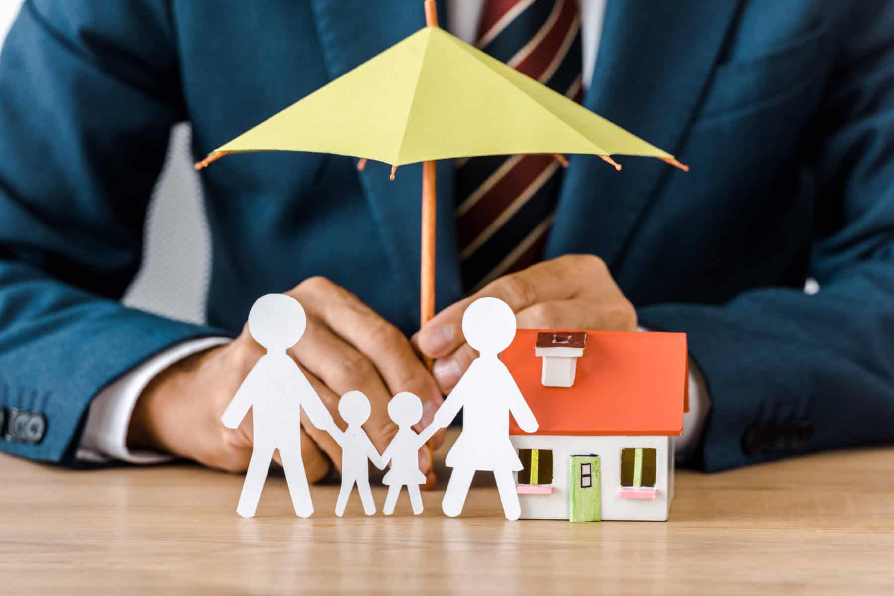 Mãos de homem seguram um chapéu miniatura que está sobre uma família de papel e uma casa.