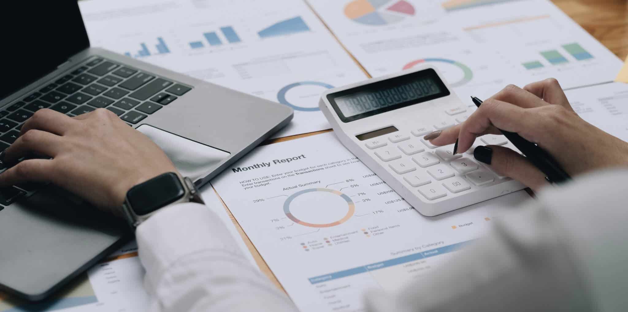 mulher sentada numa mesa a verificar faturas e a fazer contas numa calculadora ao mesmo tempo que vai apontando as despesas no computador
