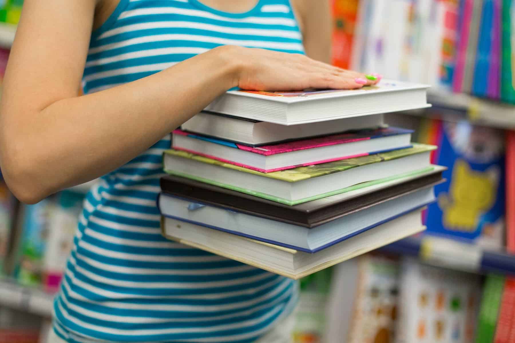 rapariga com vários livros na mão numa livraria a ilustrar os manuais escolares grátis