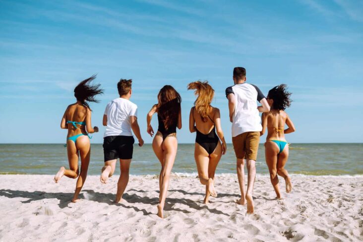 grupo de amigos a correr na praia em direção à água, num período de férias