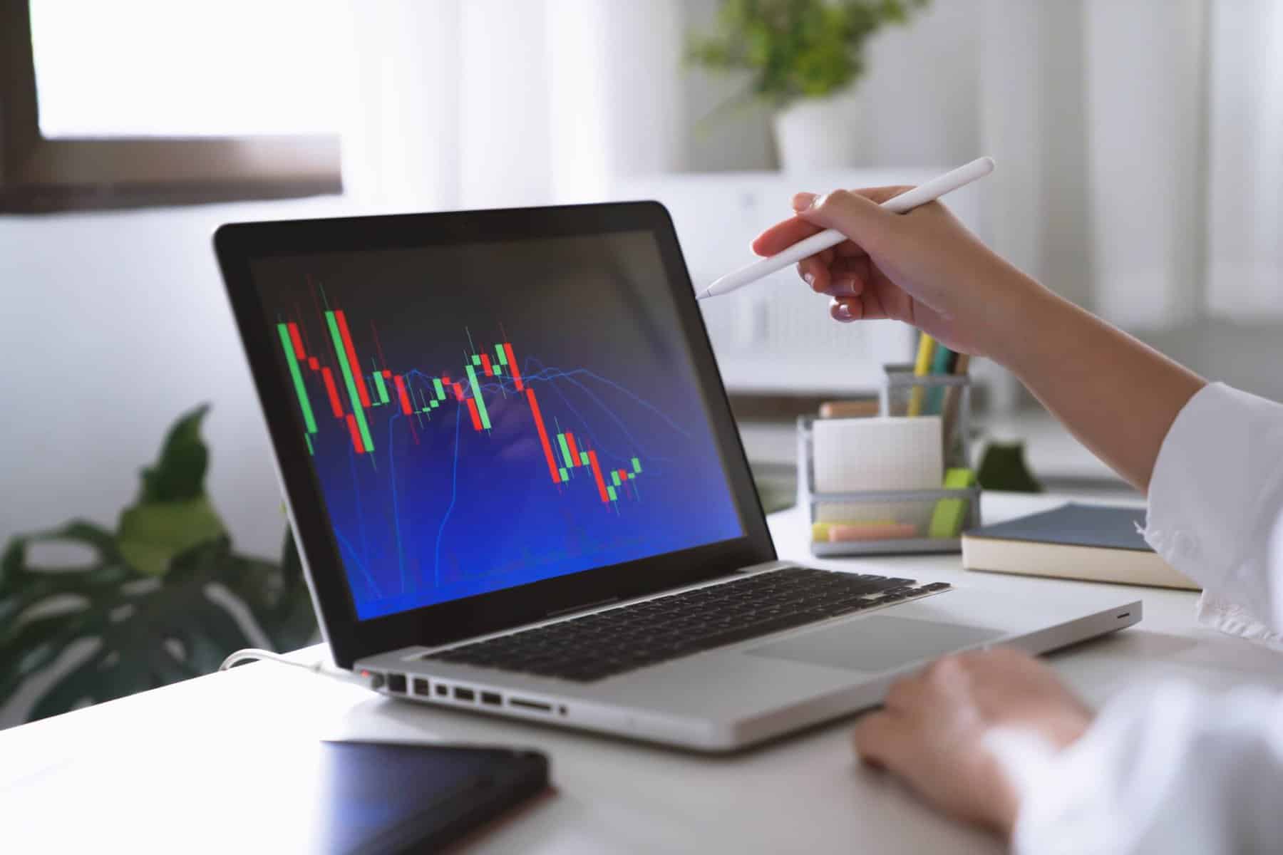 Mãos de mulher a apontar para um computador. No ecrã é possível ver um gráfico com o desempenho de um investimento realizado