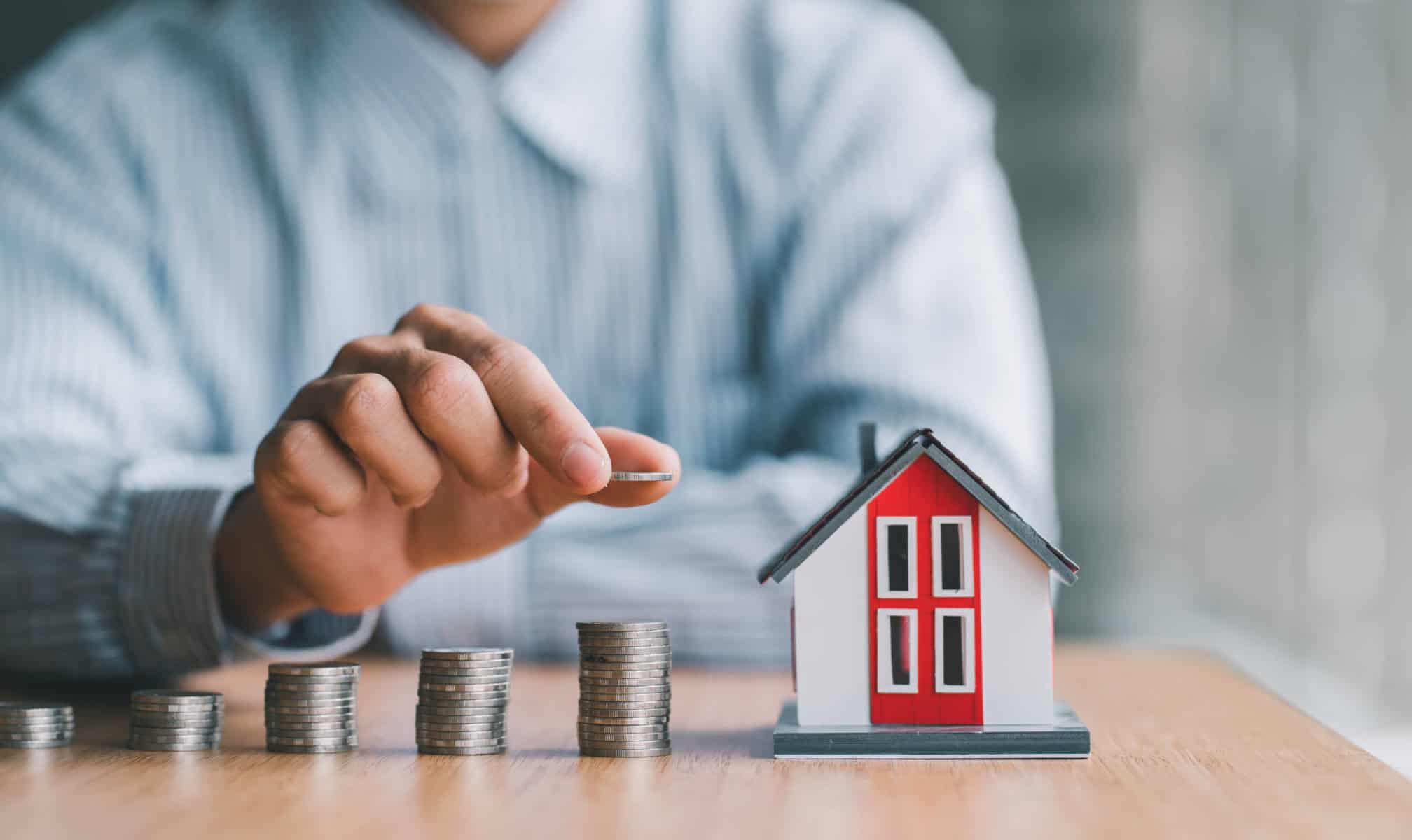 homem a colocar moedas na secretária junto a uma casa a ilustrar como poupar nos seguros do crédito habitação
