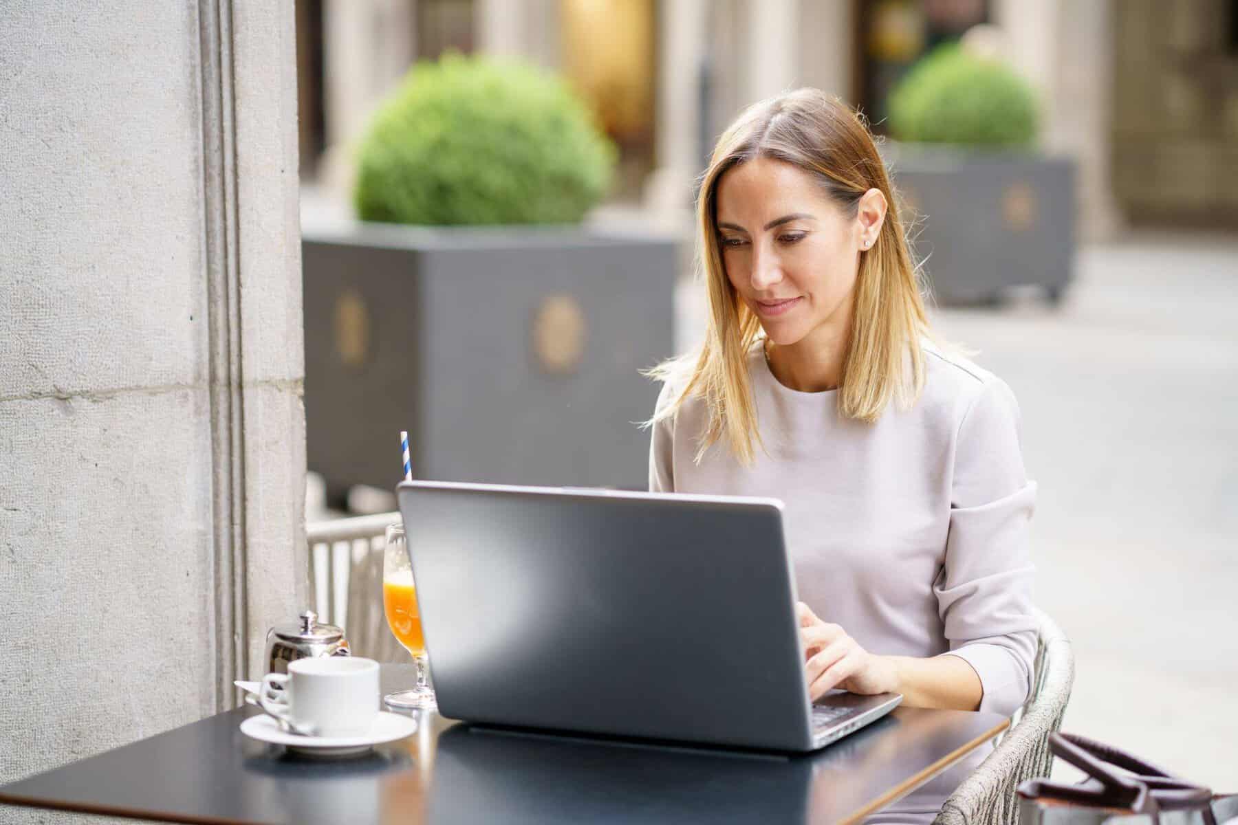 mulher sentada numa esplanada ao computador. Imagem a ilustrar texto sobre a relação entre trabalhador independente e segurança social