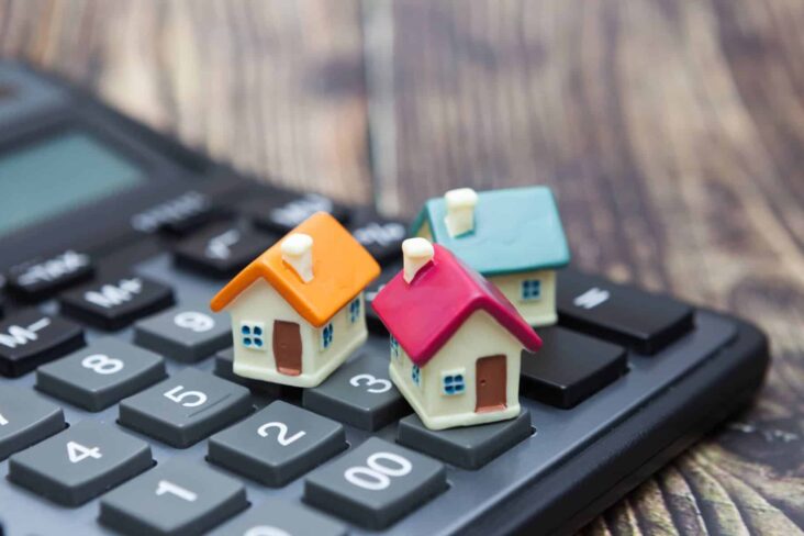 miniaturas de casas coloridas pousadas em cima de uma calculadora, numa alusão às contas que se têm de fazer para se comprar uma casa, nomeadamente de impostos.