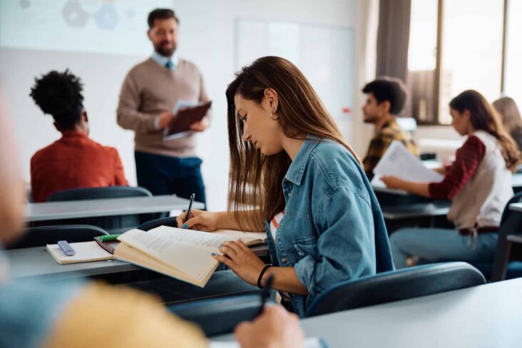 Vários estudantes universitários numa aula com um professor. Alusão aos apoios aos estudantes bolseiros deslocados.