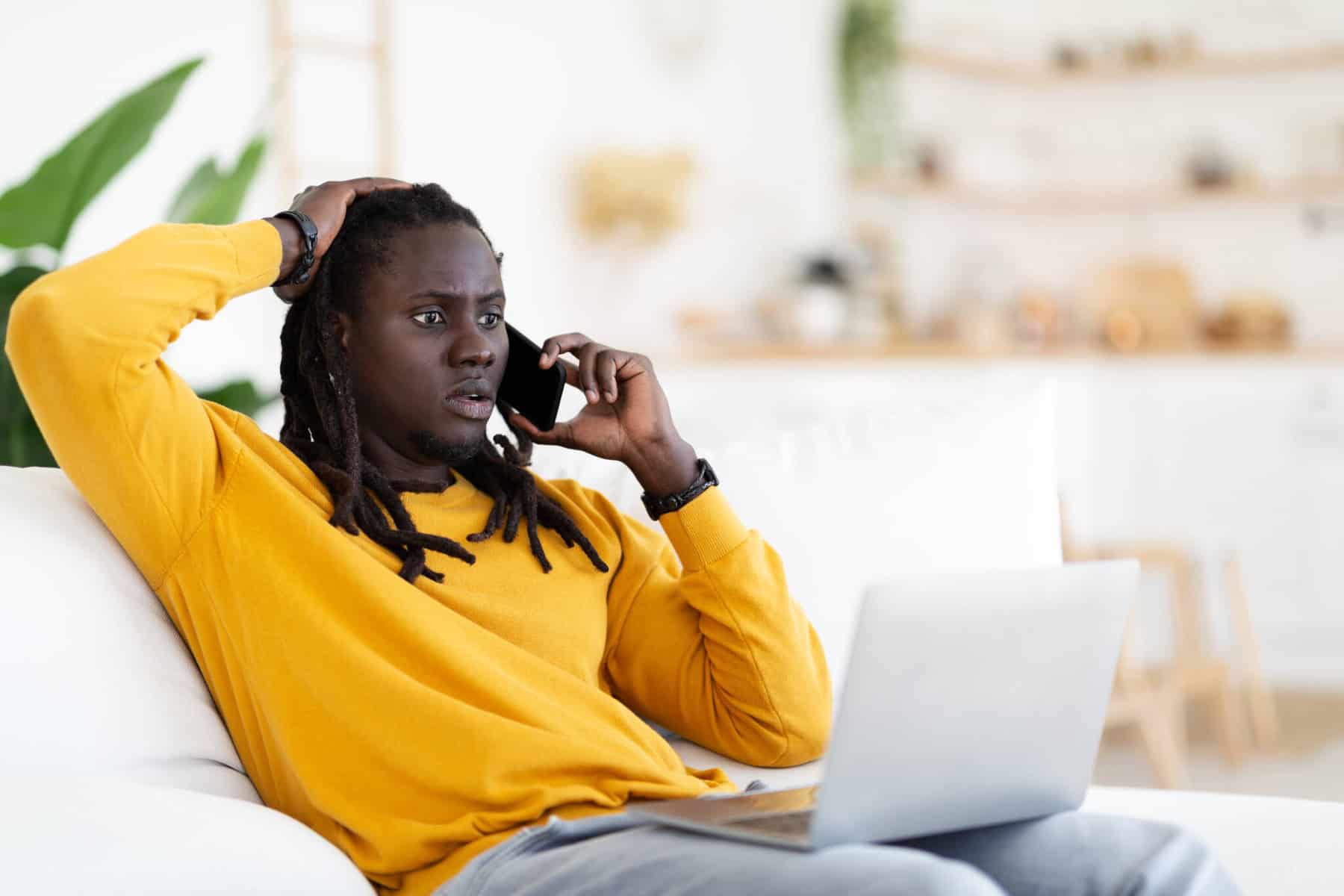 homem sentado no sofá a falar ao telefone com um computador ao colo a ilustrar as novas burlas financeiras realizadas por chamada