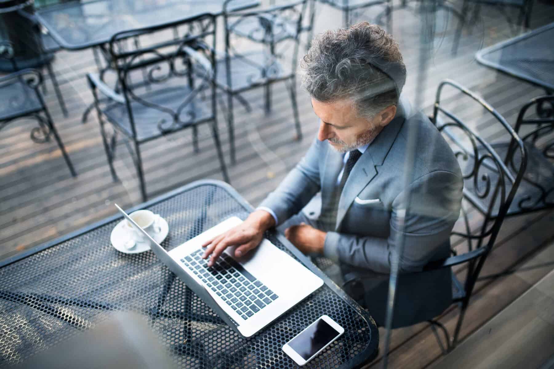 Homem sentado numa esplanada a beber café enquanto consulta no seu computador as condições para contratar um crédito pessoal online