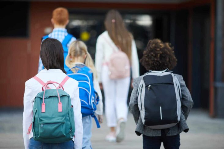 Várias crianças, com mochila às costas, deslocam-se para dentro da escola, numa alusão ao regresso às aulas