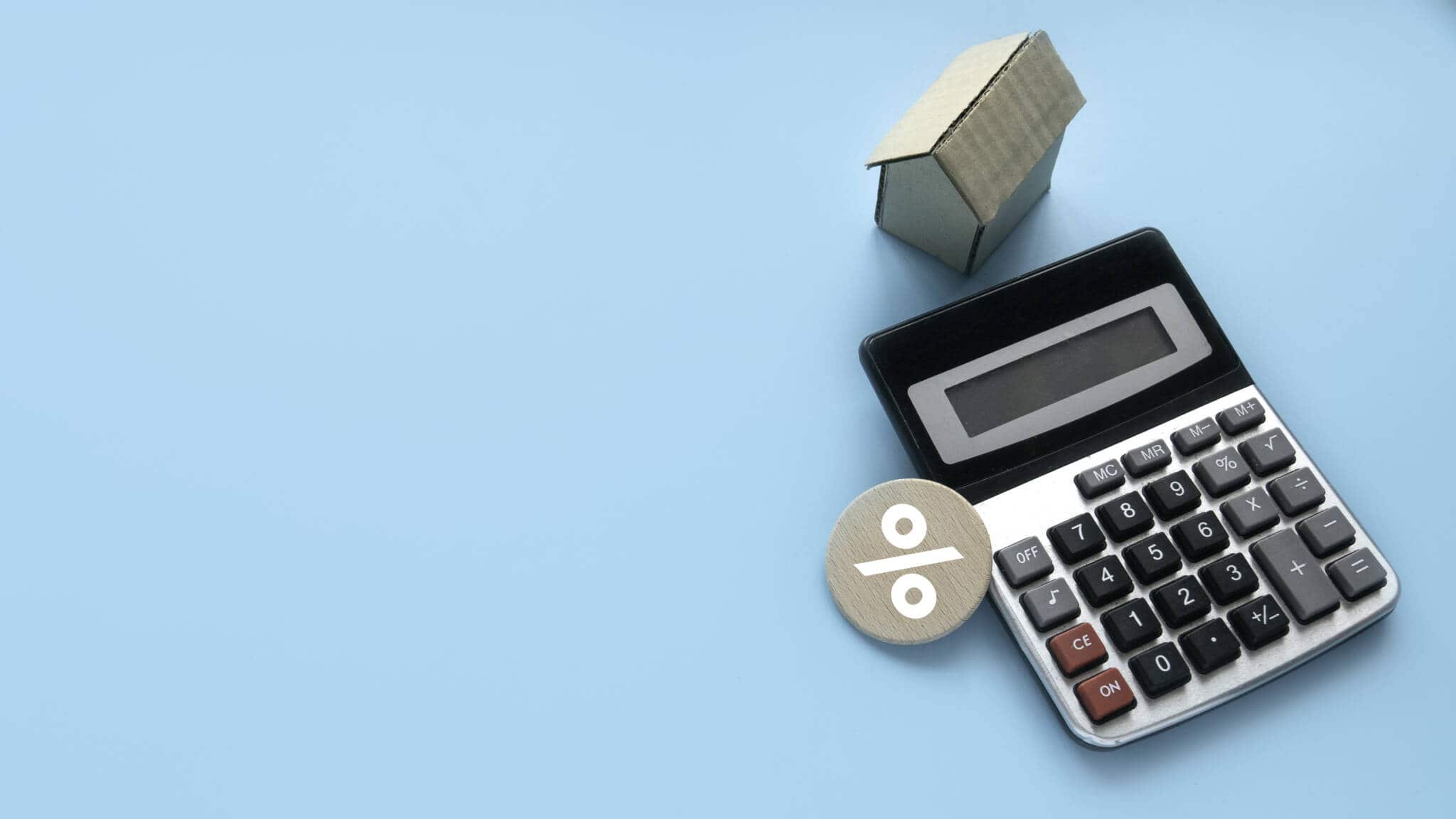 calculadora com maquete de casa e símbolo de percentagem