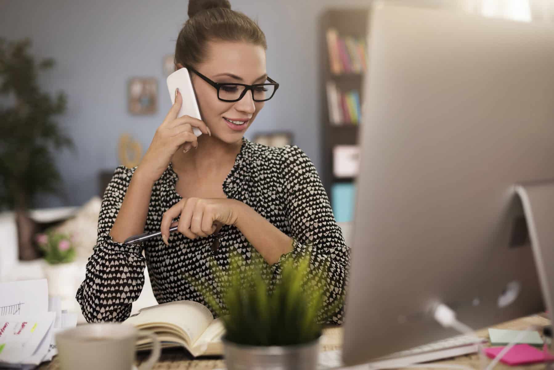 sócia de uma empresa frente ao computador enquanto está ao telemóvel a informar-se como abrir uma conta empresarial