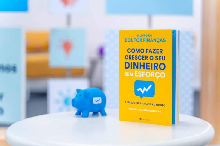 Livro Como fazer crescer o seu dinheiro sem esforço , do Doutor Finanças, em cima de uma mesa. Ao seu lado um porquinho mealheiro com a marca Doutor Finanças