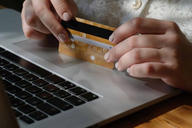 mulher com cartão bancário na mão ao pé do computador para cancelar débito direto