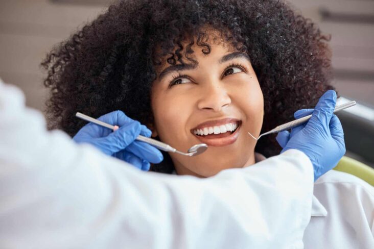 Jovem sentada numa cadeira de dentista com um rasgado sorriso, enquanto o médico se prepara para examinas a sua boca.