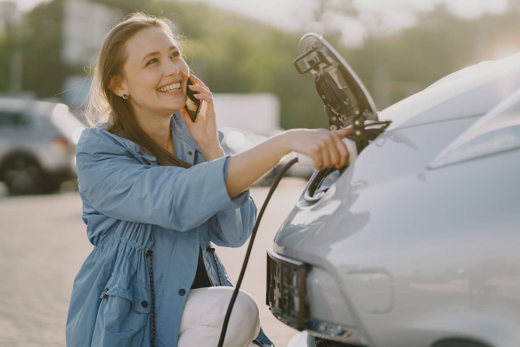 Mulher feliz a carregar o seu carro elétrico e a falar com a seguradora
