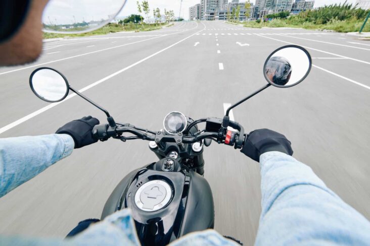 Jovem conduz uma moto numa estrada com várias faixas de rodagem.