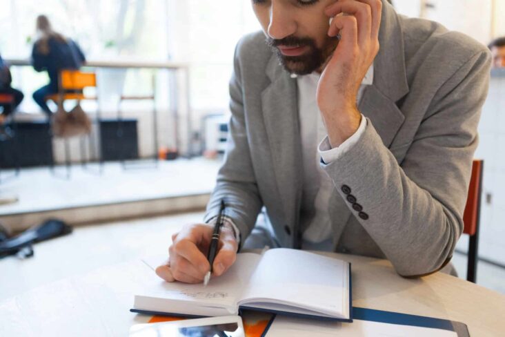 Trabalhador sentado numa mesa, a apontar dados num caderno, enquanto fala ao telemóvel