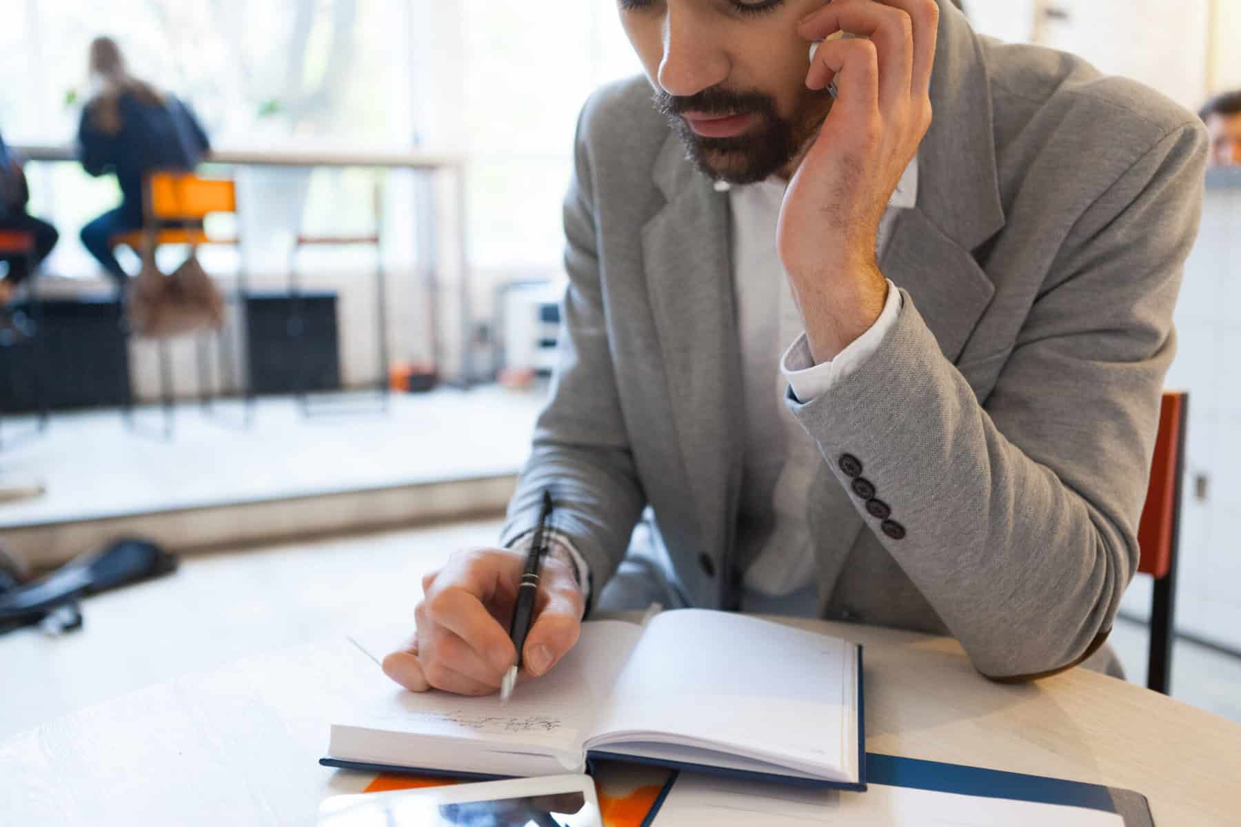 Trabalhador sentado numa mesa, a apontar dados num caderno, enquanto fala ao telemóvel