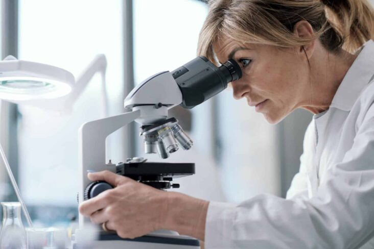 Cientista sentada a olhar pelo microscópio a evocar o reconhecimento das qualificações profissionais