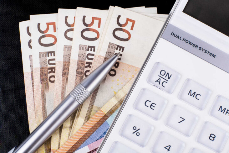 Várias notas de 50 euros pousadas em cima de uma mesa. Por cima delas surge uma caneta um lápis e uma máquina calculadora.
